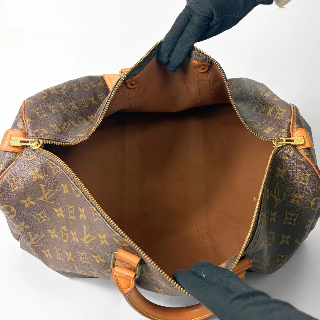 Brown hand bag with orange accents and a prominent logo pattern on a white background