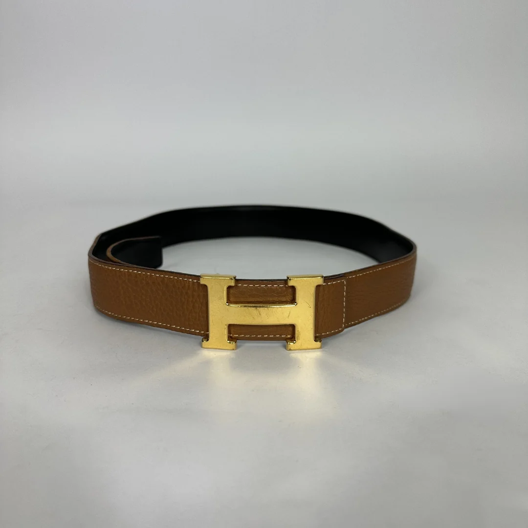 A classic brown leather belt with a gold-tone H buckle, displayed on a neutral light gray background.