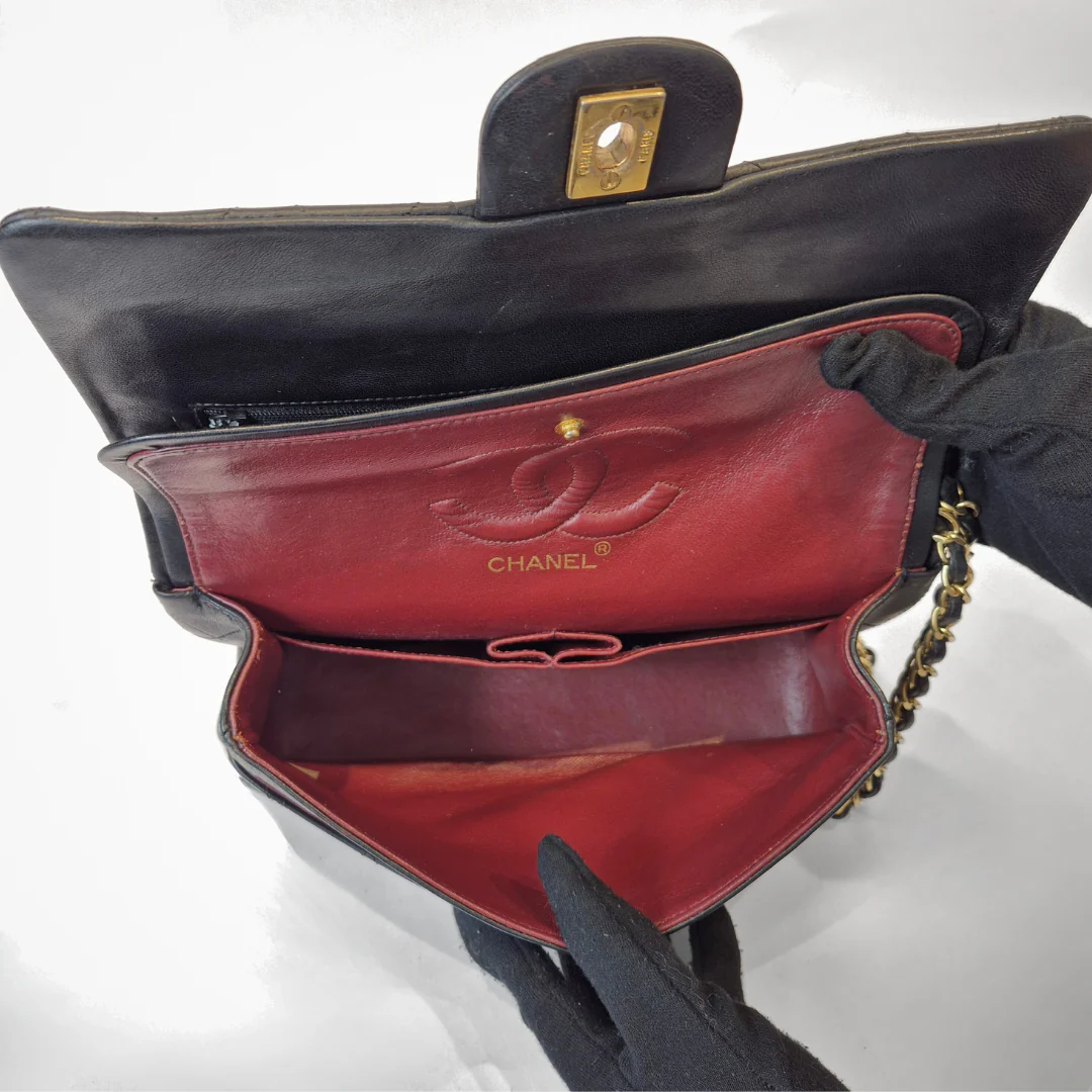 Black leather handbag with red interior, featuring the Chanel logo, held by a gloved hand.
