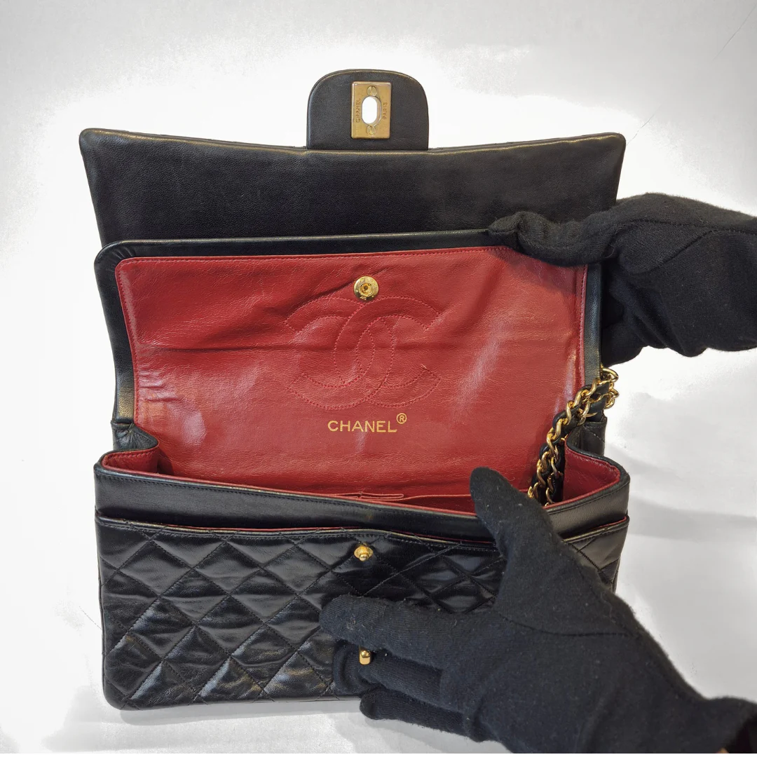 Black quilted handbag with red interior, featuring Chanel logo, held open by a gloved hand.