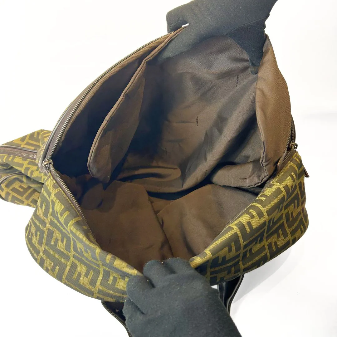 Person opening a green and brown patterned backpack with a jacket inside on a white background