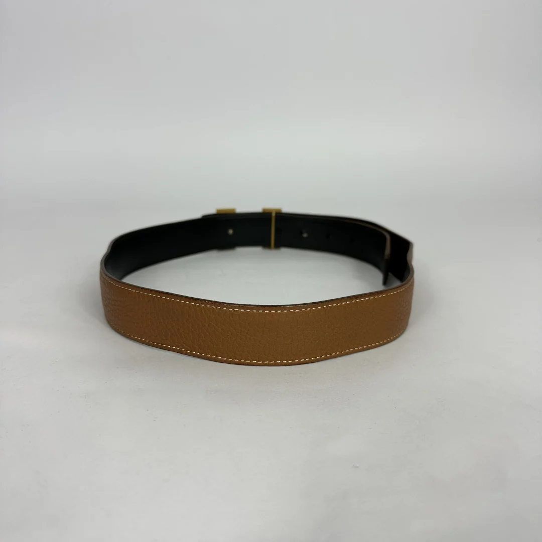 A tan textured leather belt with white contrast stitching and a black interior lining, shown on a neutral light gray background.