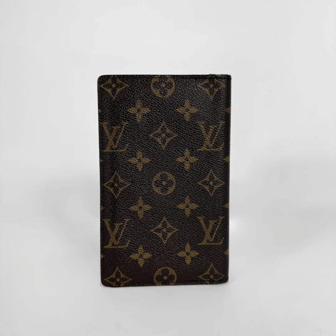 A Louis Vuitton monogram card holder or passport cover made of dark brown coated canvas with the classic tan/gold LV monogram pattern, standing upright on a light gray background.