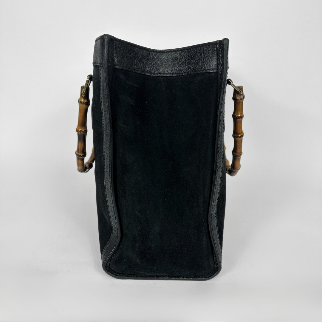 Black handbag with gold bamboo handles on a white background