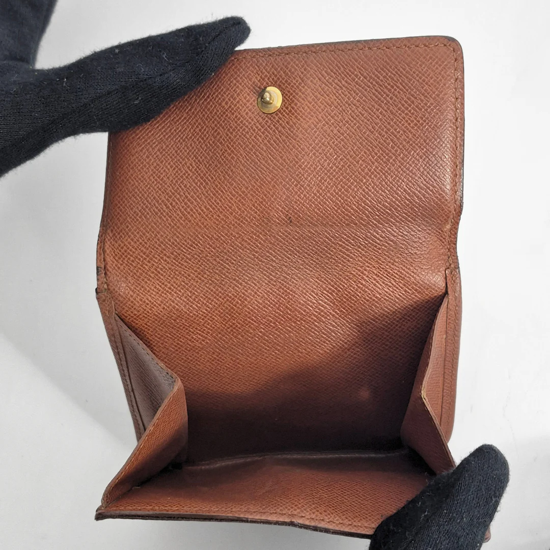 Brown leather wallet held by a gloved hand on a light gray background