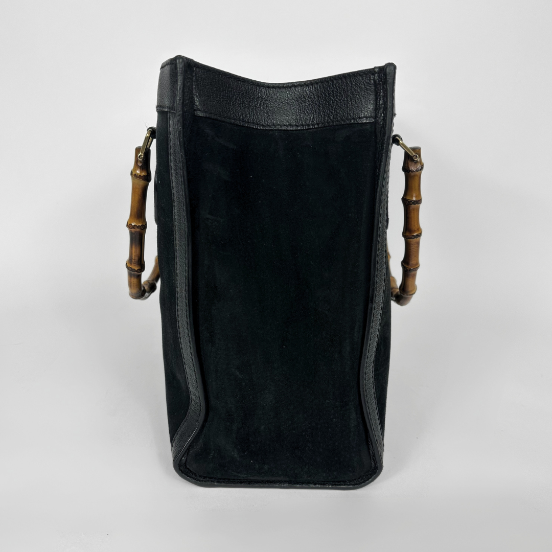 Black handbag with gold bamboo handles on a white background