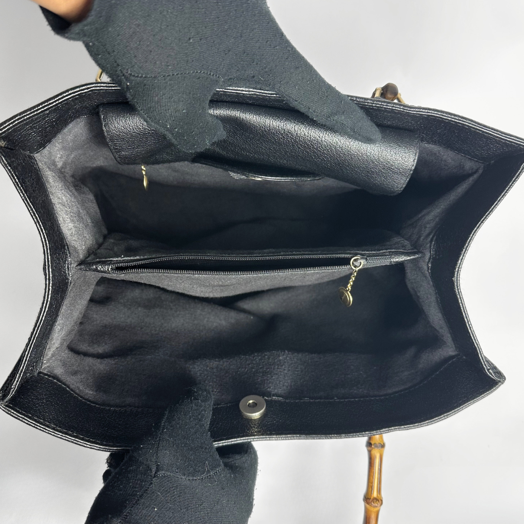Black handbag with gold bamboo handles on a white background