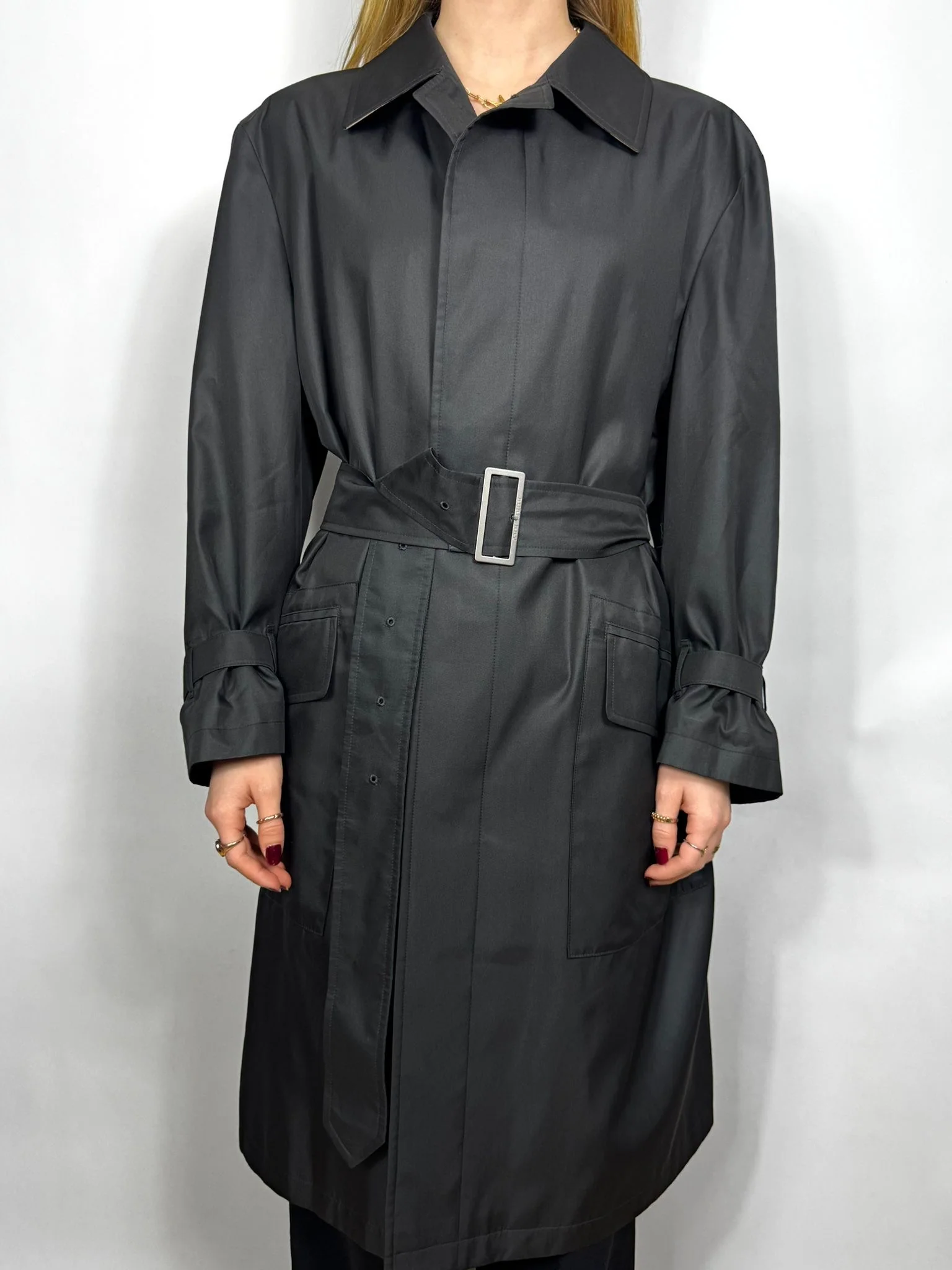 Person wearing a long black coat with a belt on a white background