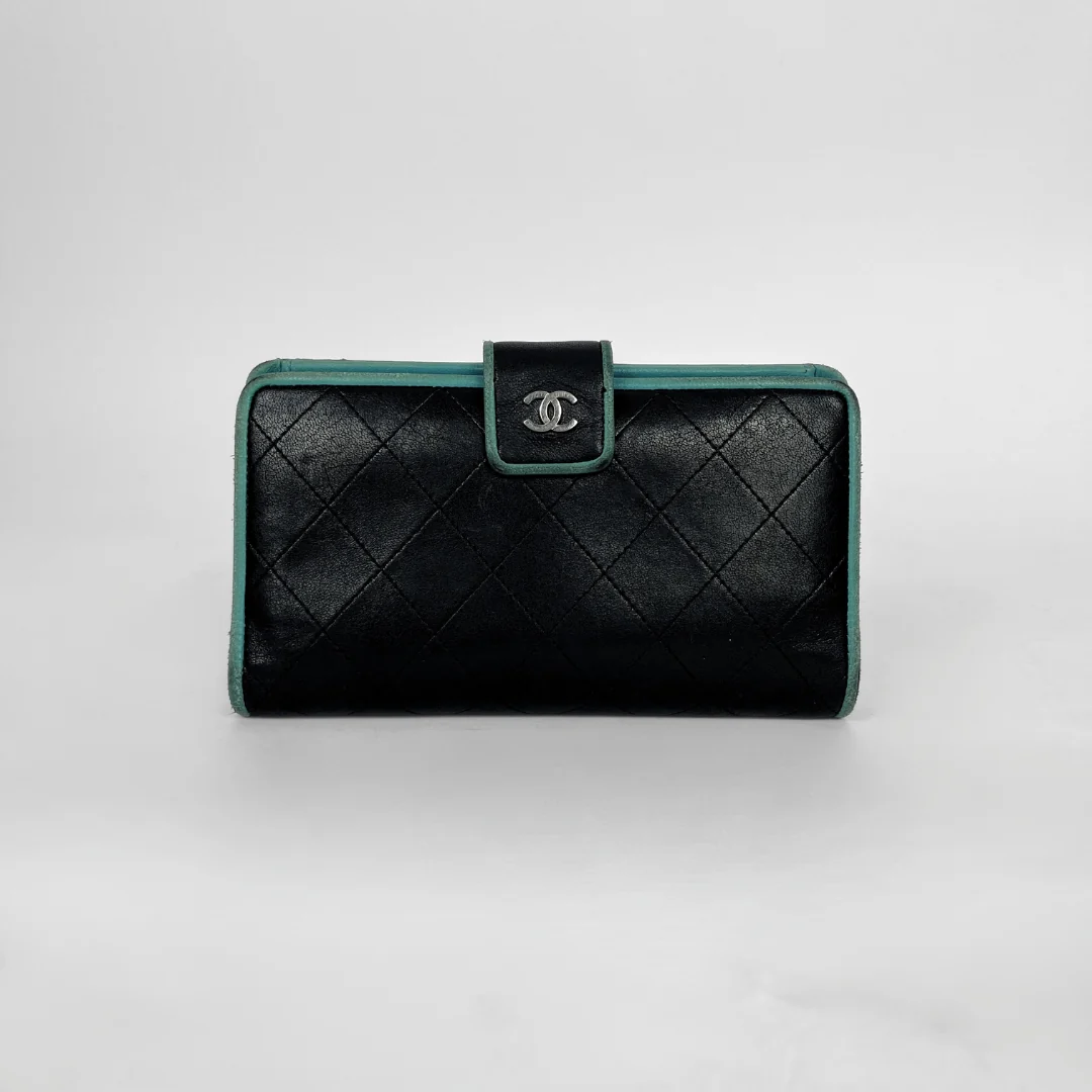 A black quilted leather clutch wallet with a silver-tone interlocking CC logo on the front flap, accented by a teal-green trim.