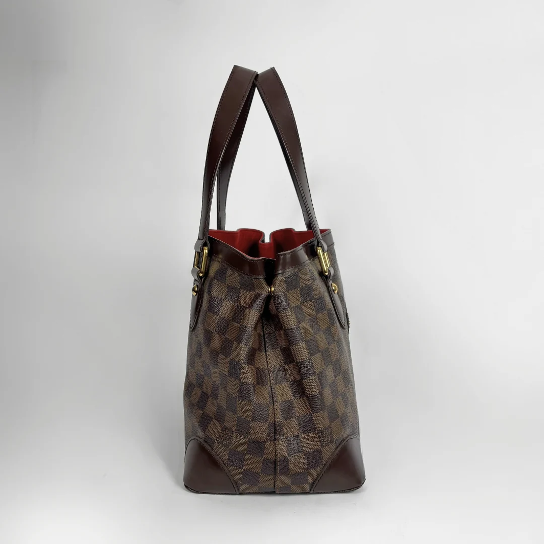 A brown checkered canvas tote bag with dark brown leather handles and trim, shown against a neutral light gray background.