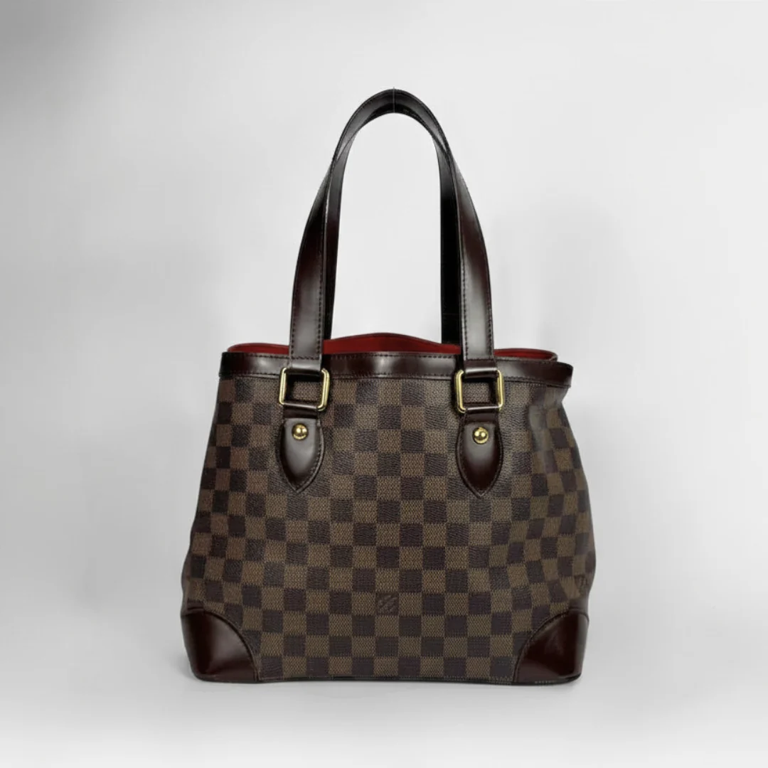 A Louis Vuitton handbag in Damier Ebene canvas with dark brown leather handles and trim, featuring gold-tone hardware, set against a neutral light gray background.