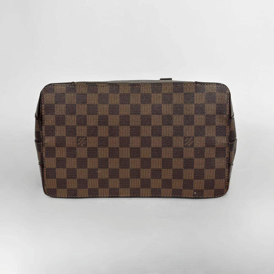 A Louis Vuitton toiletry bag in the Damier Ebene checkered canvas, showing the brown and tan patterned exterior against a light gray background.