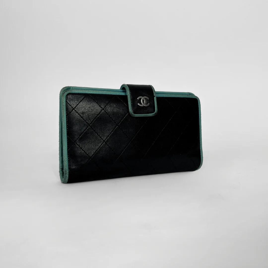 A black quilted leather wallet with green trim and a silver-tone interlocking CC logo on the front flap, photographed on a light gray studio background.