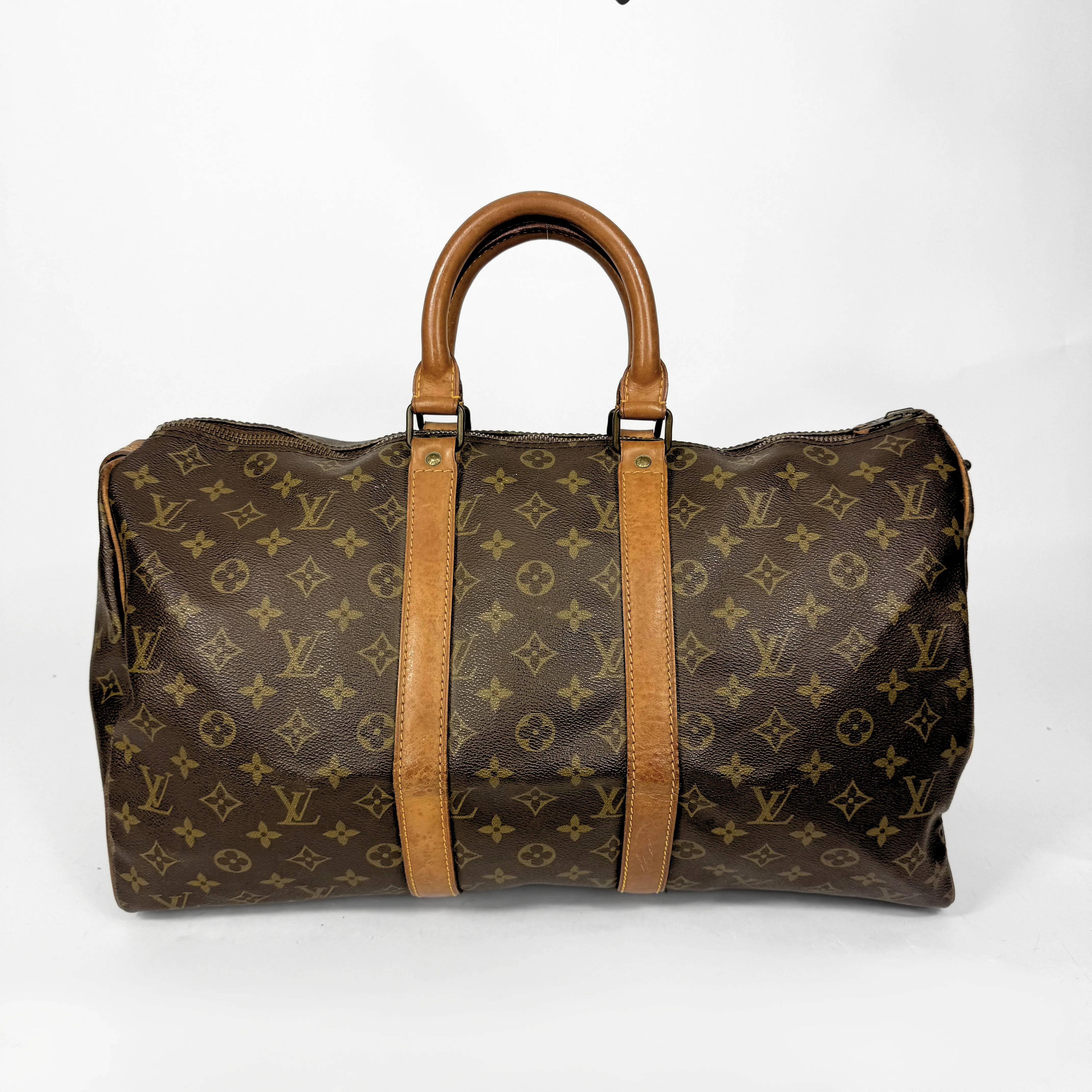 Brown Louis Vuitton monogram bag with tan leather handles and straps on a white background