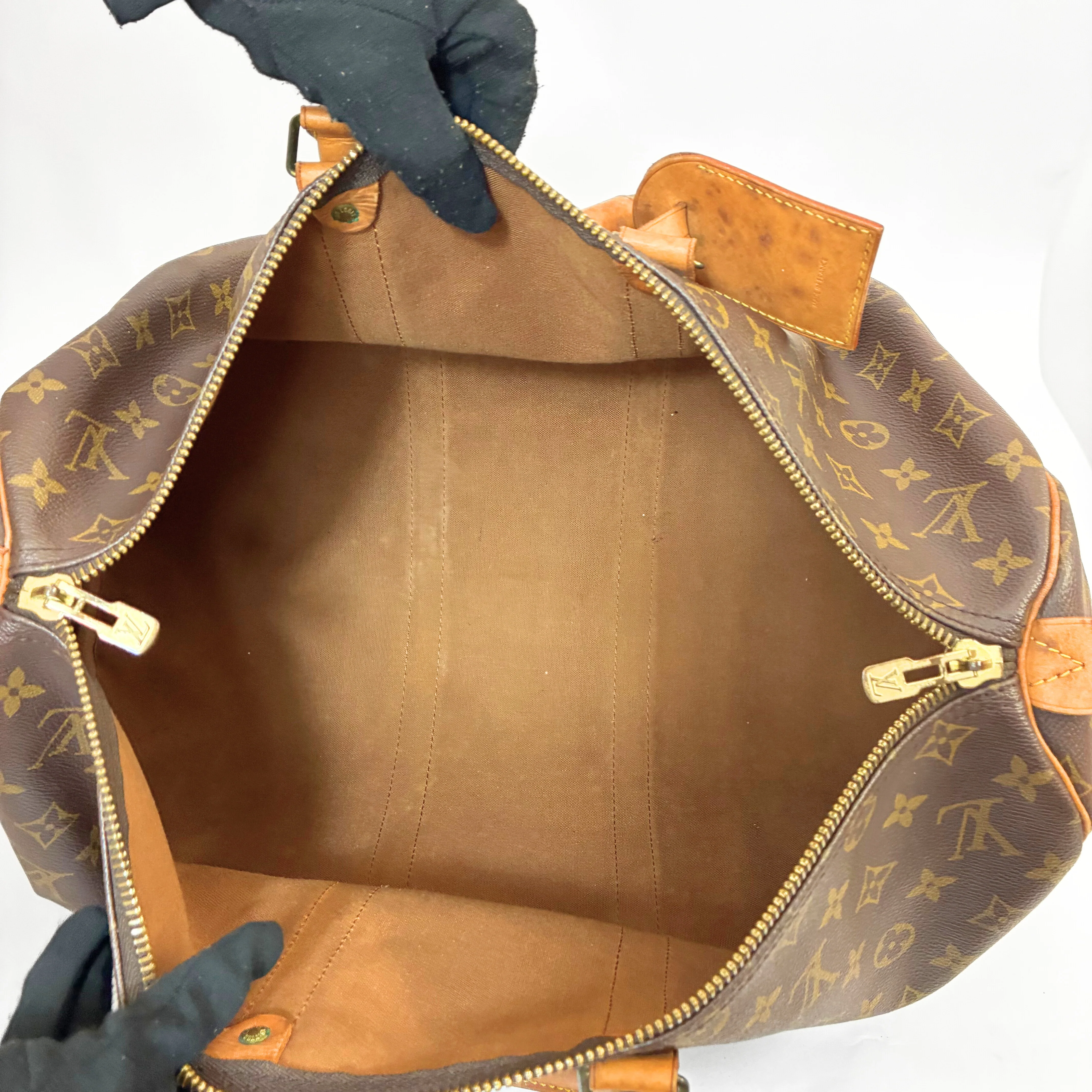 Brown leather bag with gold monogram pattern held open by black gloves on a white background
