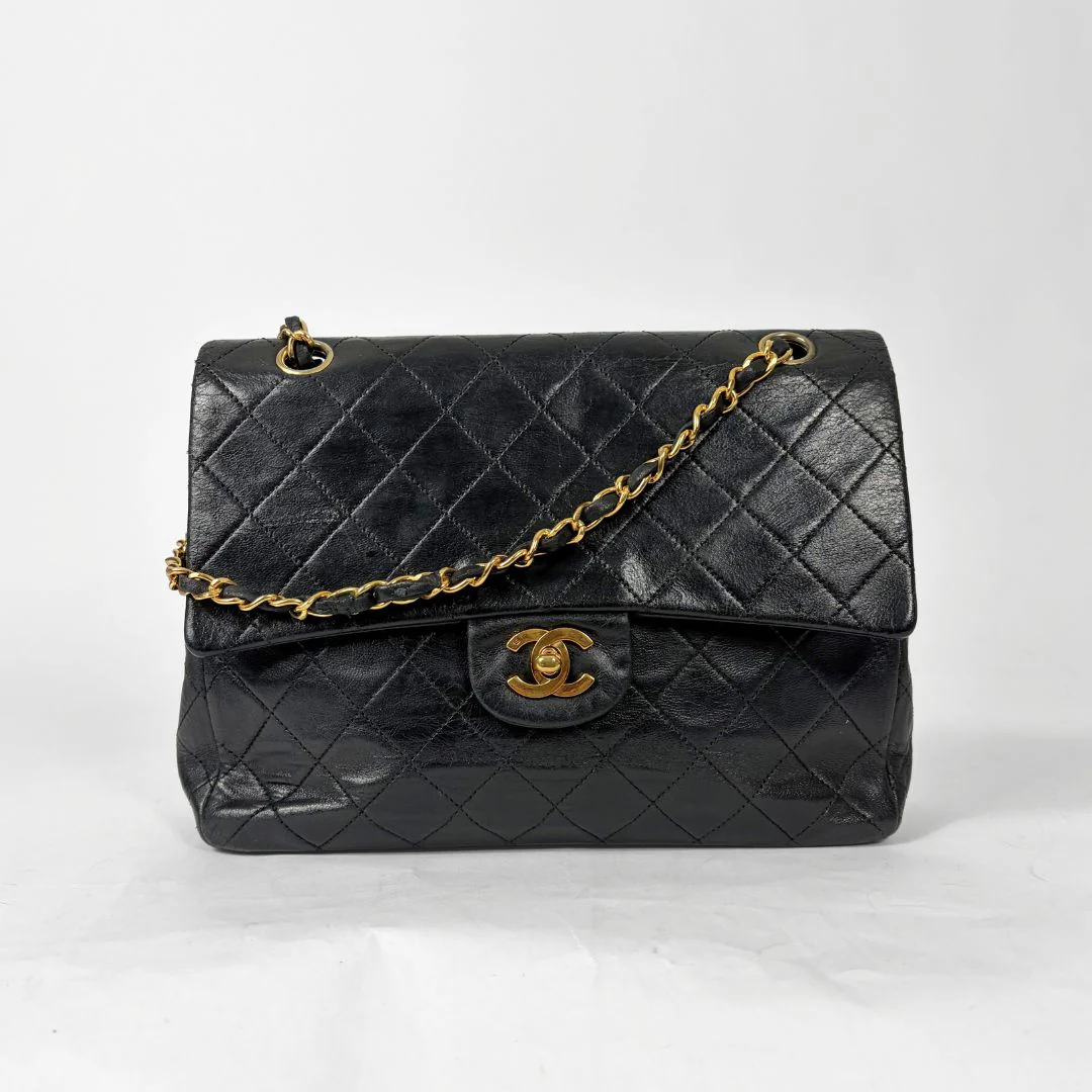 Black quilted handbag with gold chain and clasp on a white background