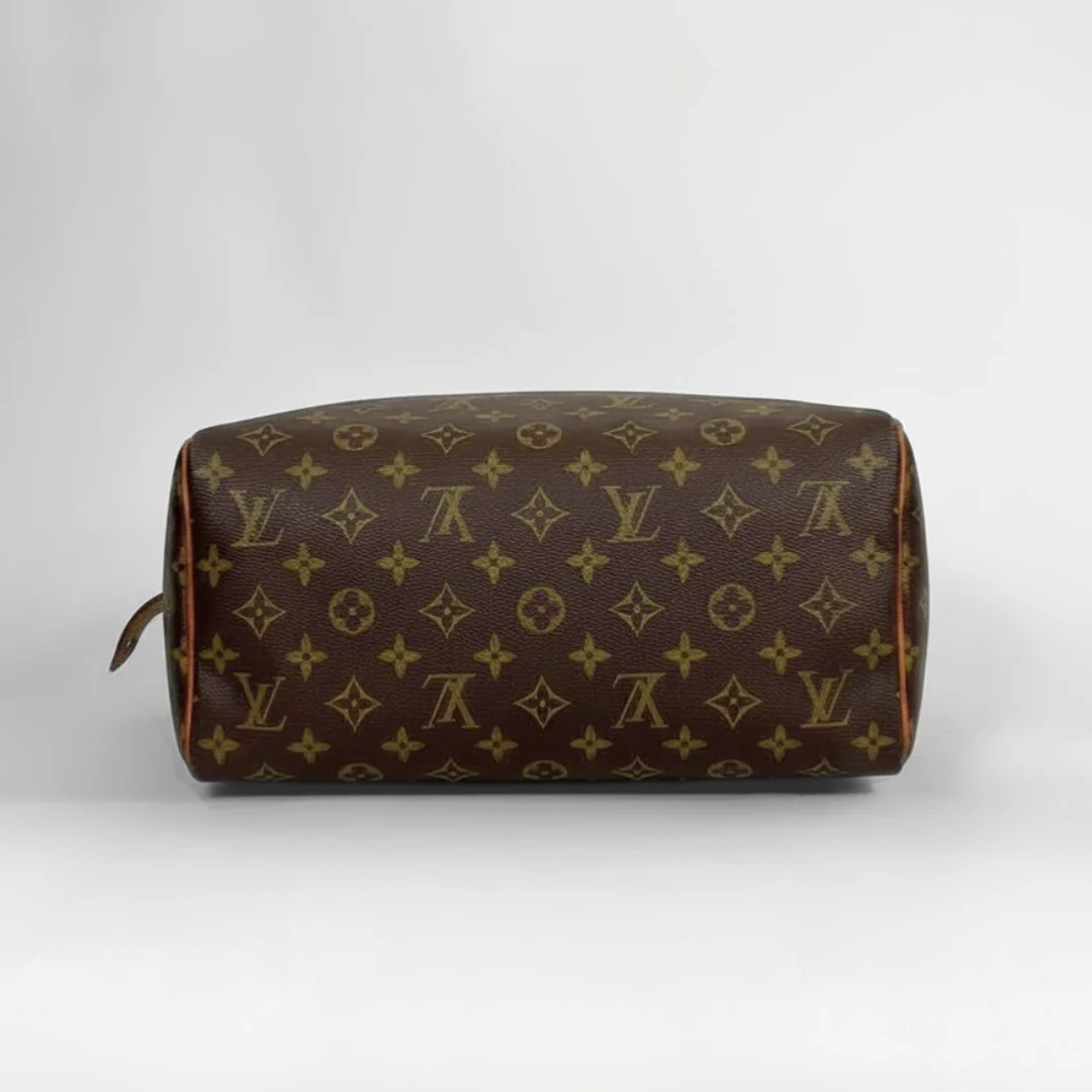 A Louis Vuitton monogram toiletry bag in brown coated canvas with gold-tone monogram print, shown from a side profile view against a light gray background.