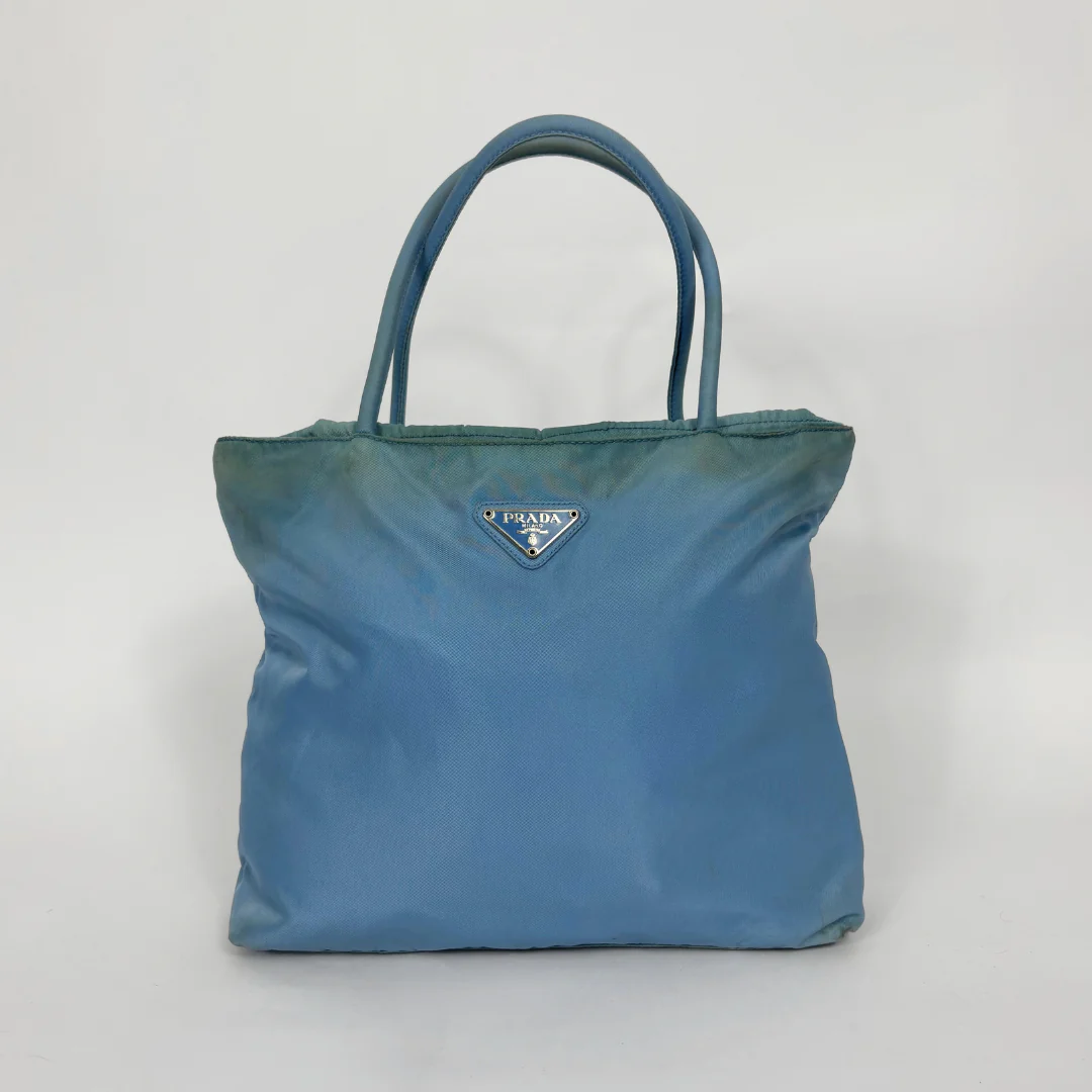 Prada light blue nylon tote bag with matching top handles and the signature enamel triangle logo.