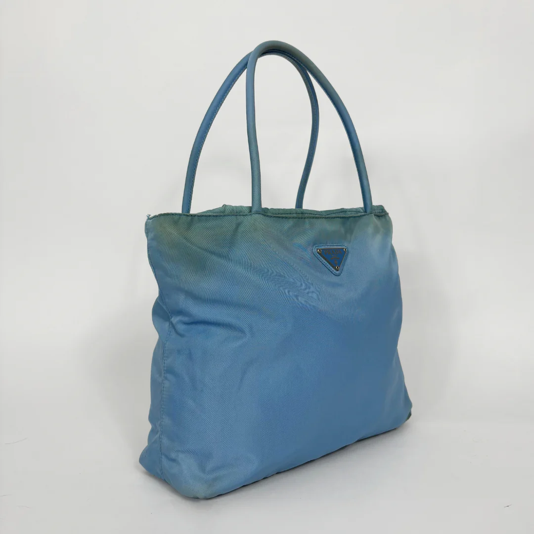 Prada light blue nylon tote bag with matching top handles and the signature enamel triangle logo.