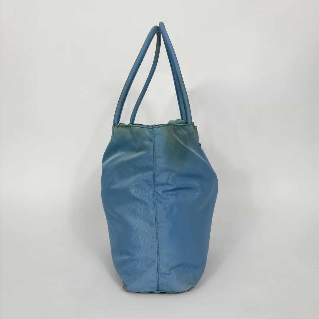 Prada light blue nylon tote bag with matching top handles and the signature enamel triangle logo.