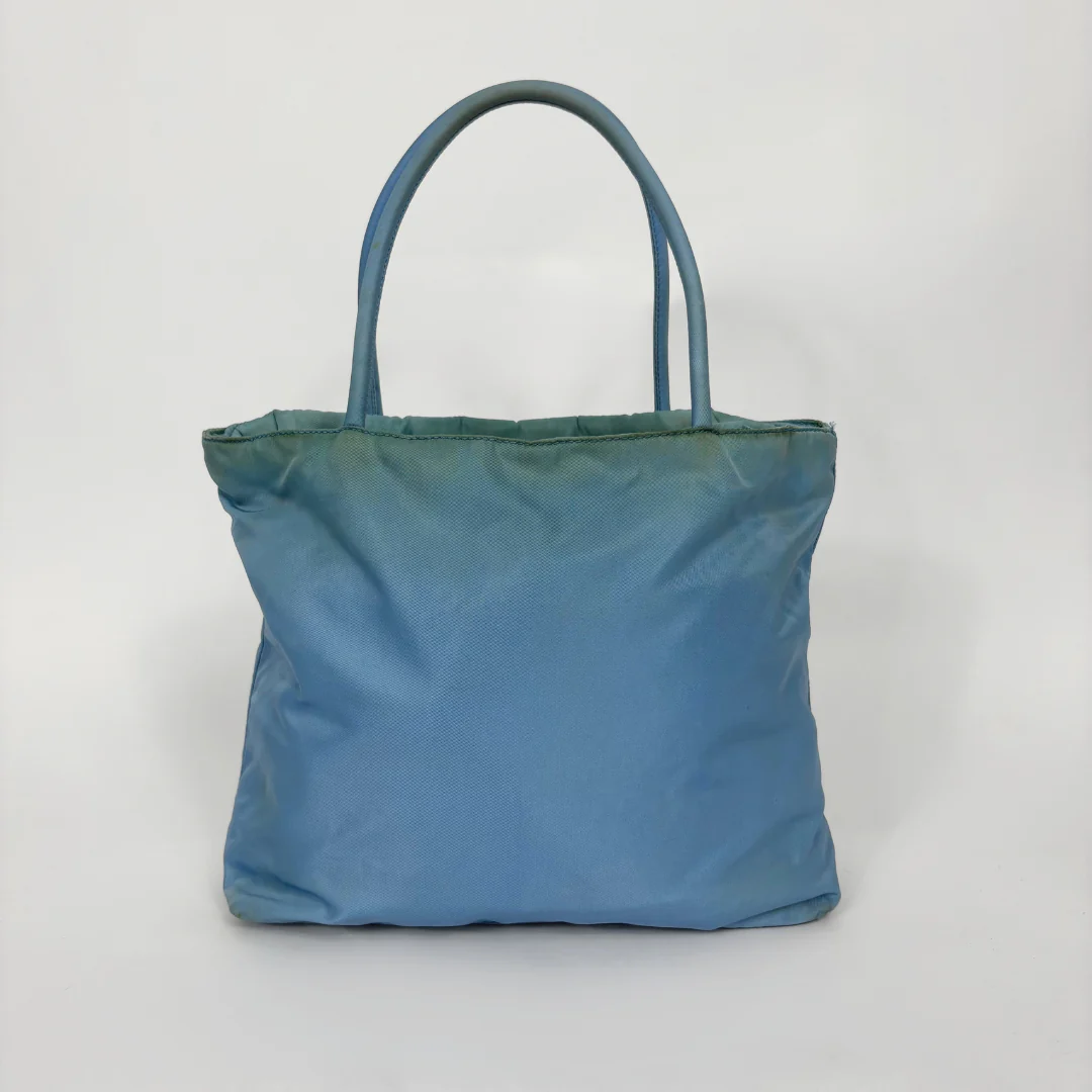 Prada light blue nylon tote bag with matching top handles and the signature enamel triangle logo.