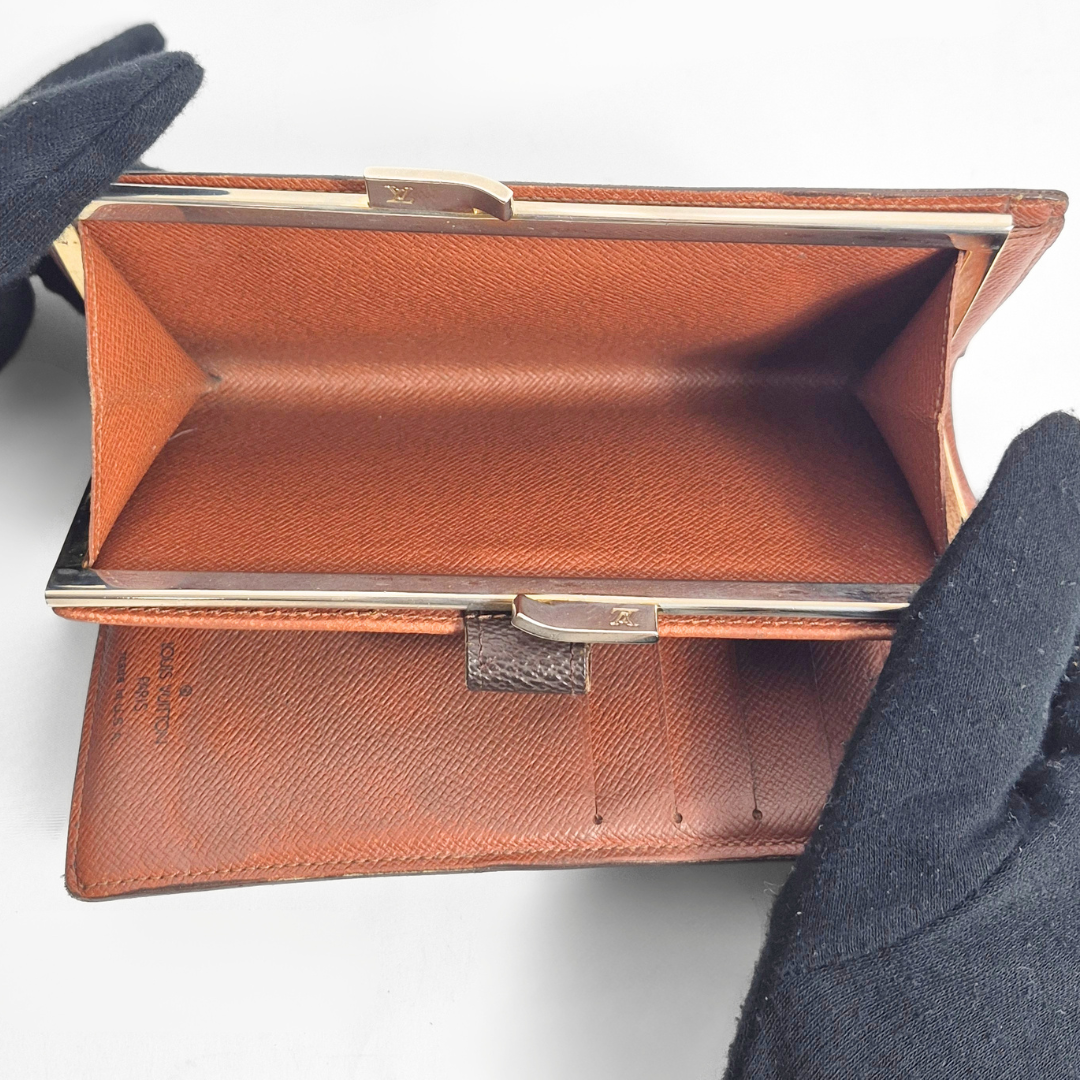 Brown leather clutch with gold trim held by a gloved hand on a light gray background