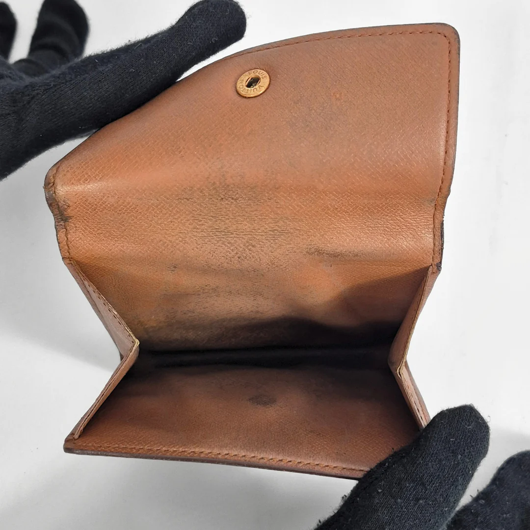 Brown leather wallet held by a gloved hand on a white background