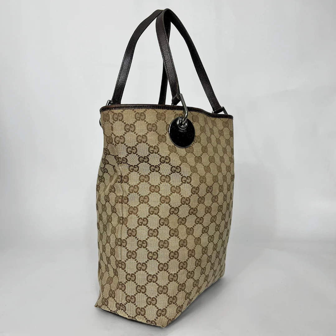 Beige and brown patterned handbag with black handles on a white background