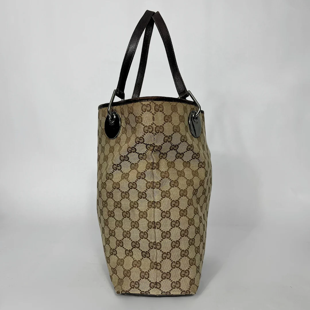 Beige and brown patterned handbag with black handles on a light gray background
