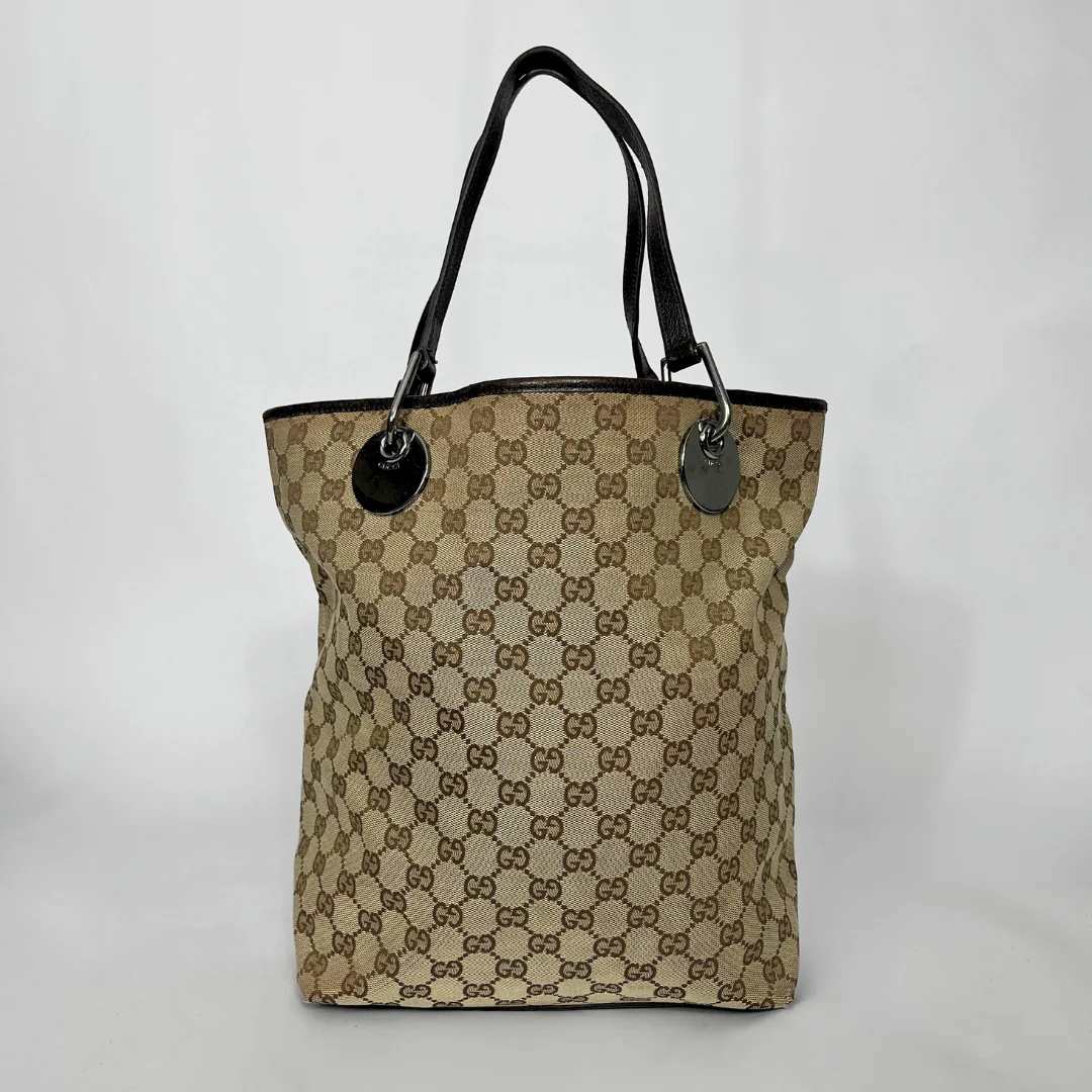 Beige and brown patterned tote bag with black handles on a white background
