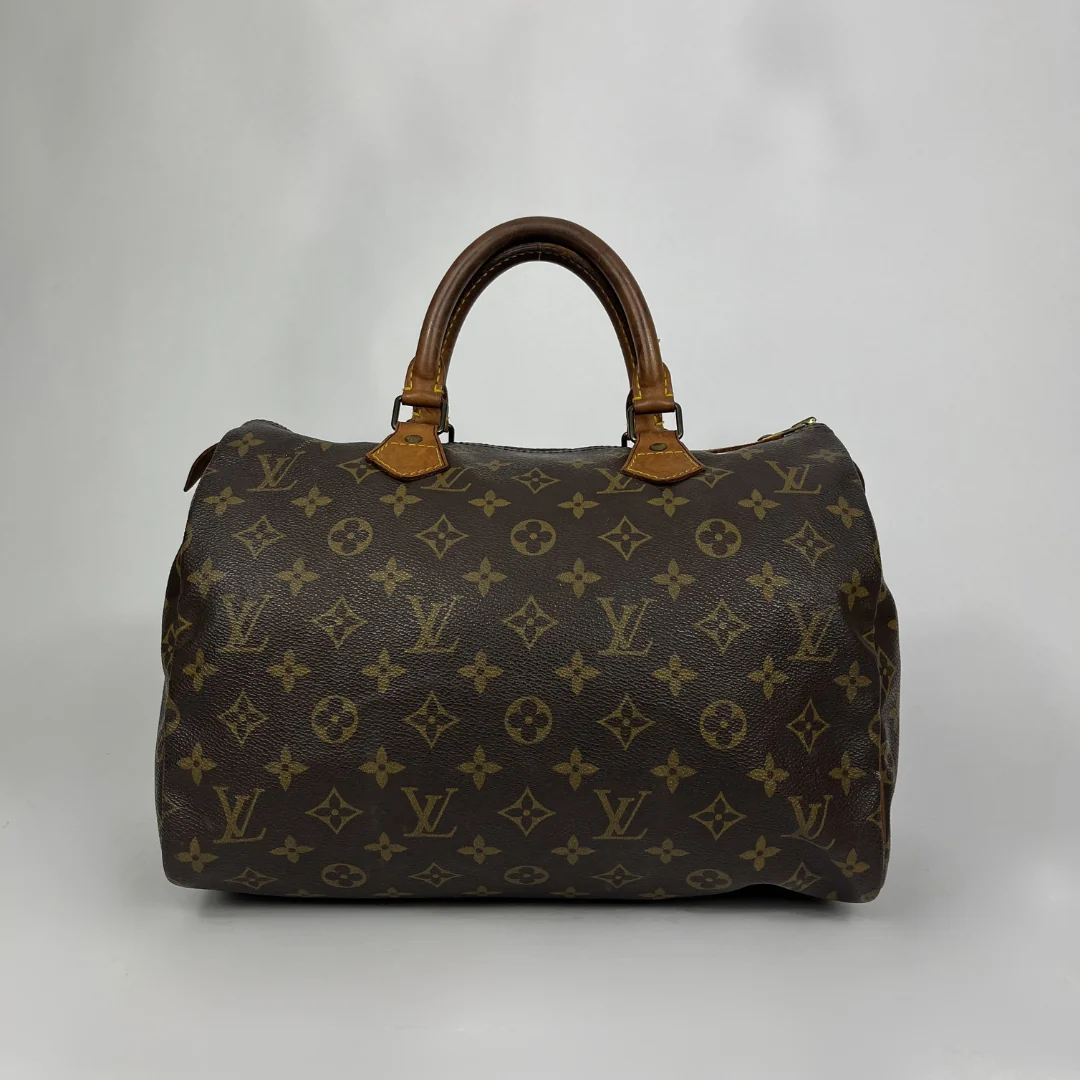 A classic Louis Vuitton monogram Speedy bag in dark brown coated canvas with tan leather handles, set against a neutral gray studio background.