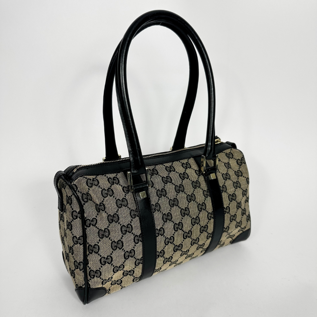 Designer handbag with black handles and trim on a light gray background