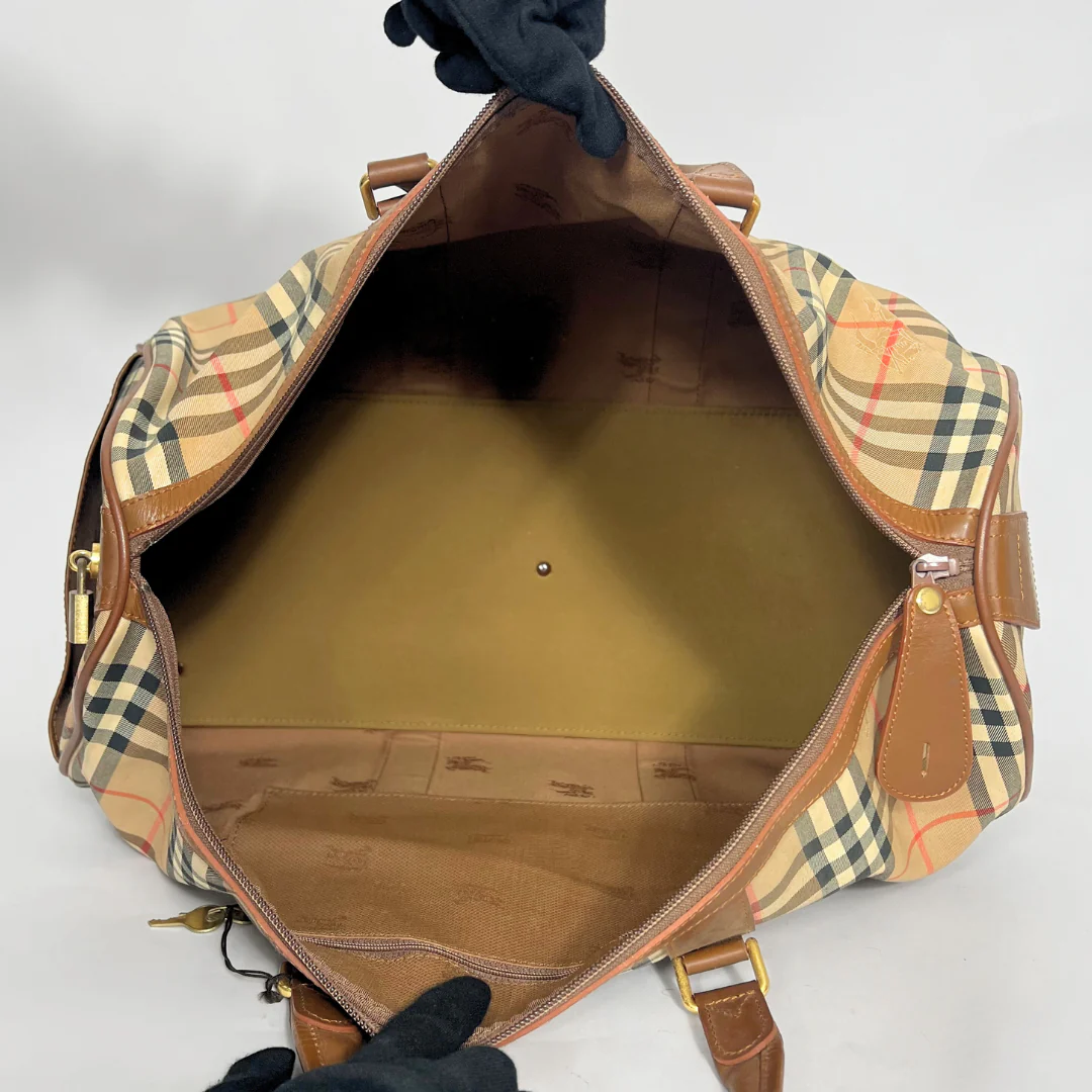 Empty checkered bag with brown interior, held open by a gloved hand on a light gray background.