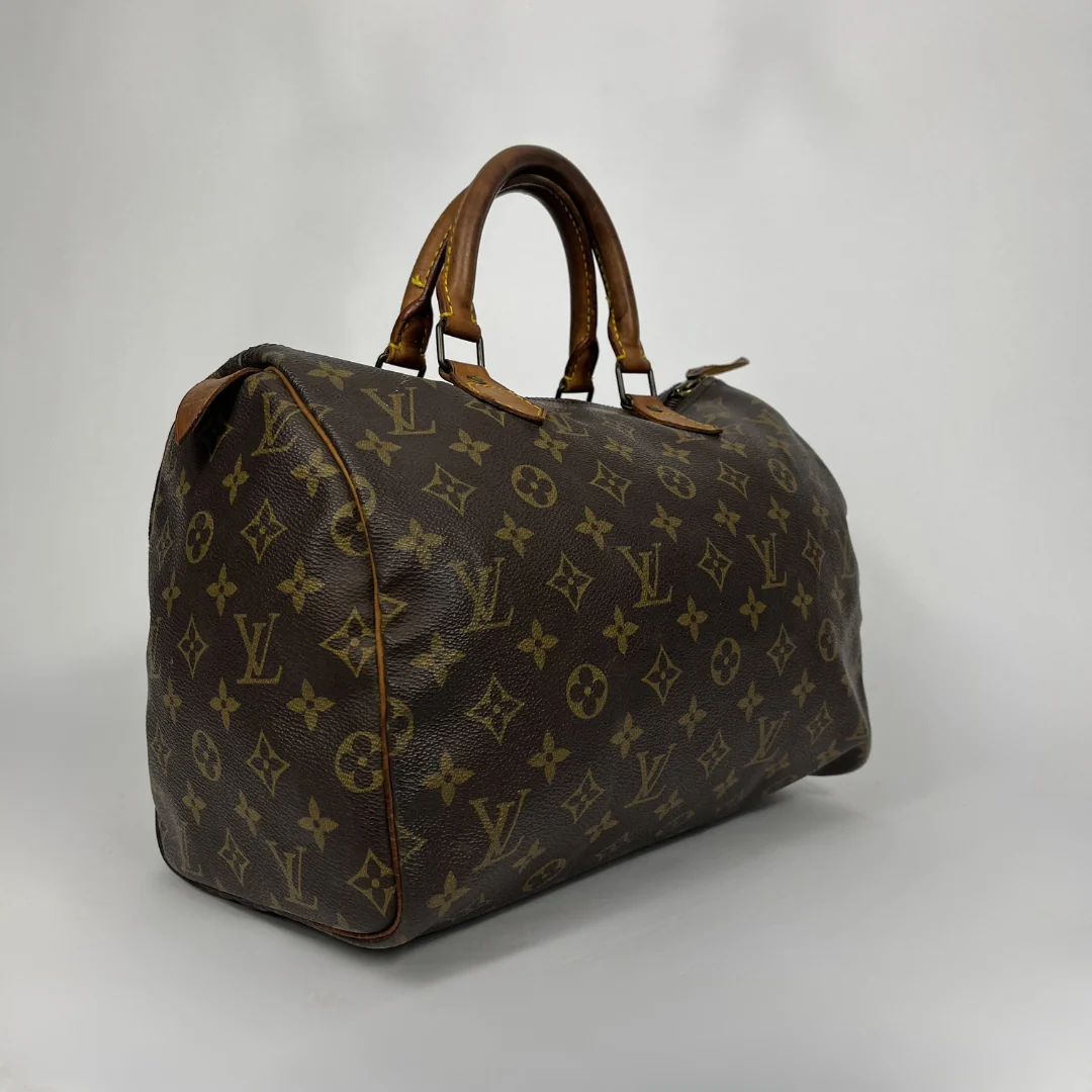 A Louis Vuitton monogram canvas speedy bag with brown leather handles and trim, photographed on a light gray studio background.