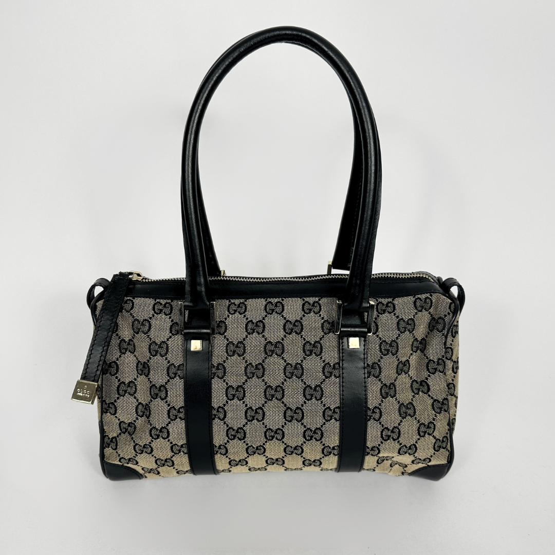 Designer handbag with black handles and trim on a light gray background