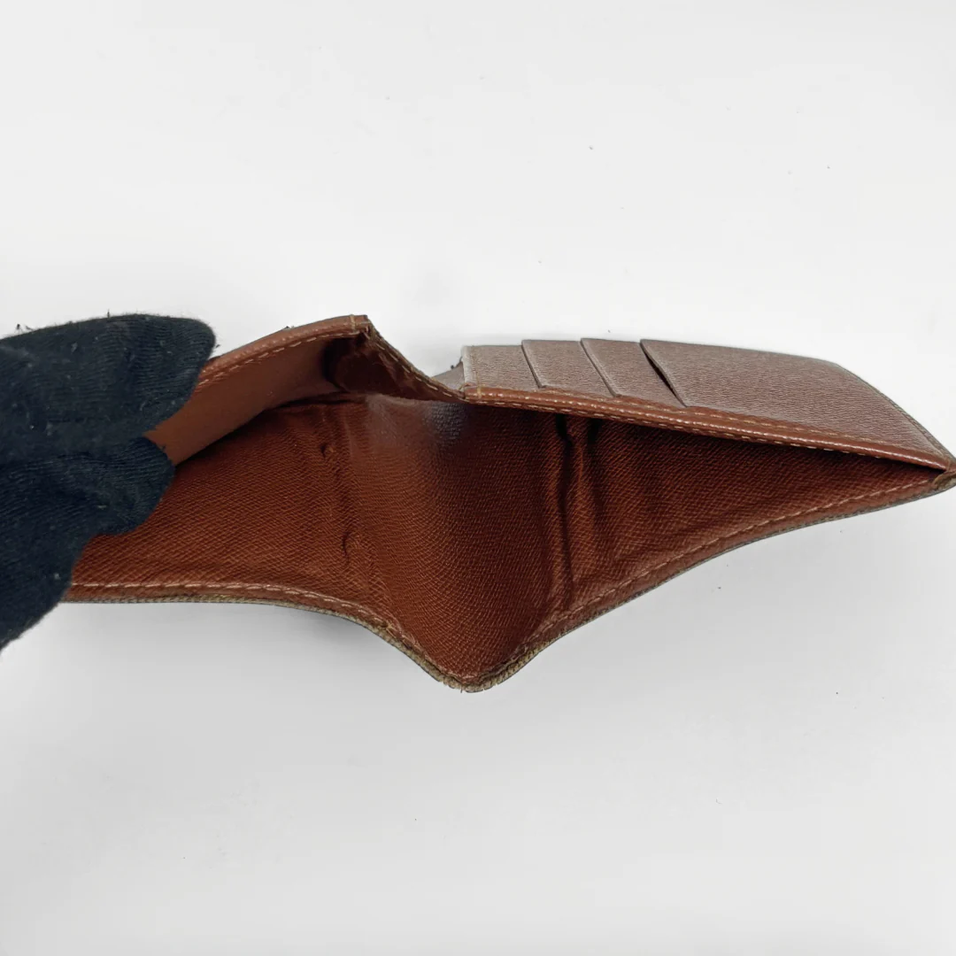 Brown leather wallet held open by a gloved hand on a white background