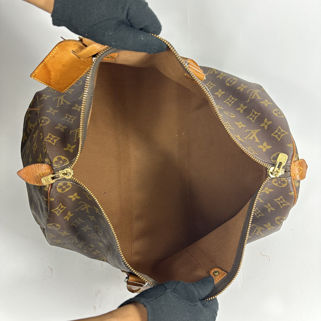Brown monogram patterned duffel bag with tan leather straps on a white background