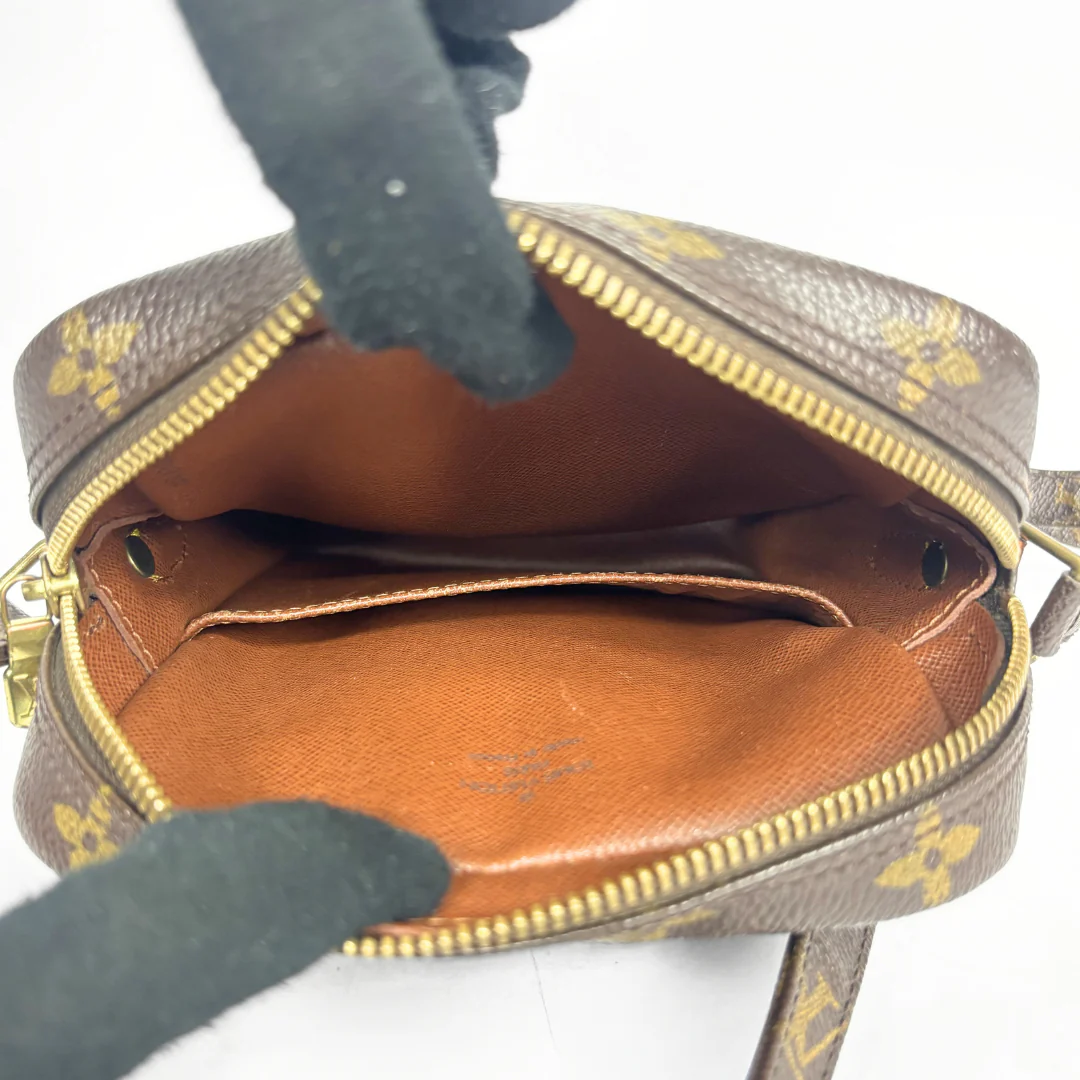 Brown handbag with gold accents being held open by a gloved hand on a white background