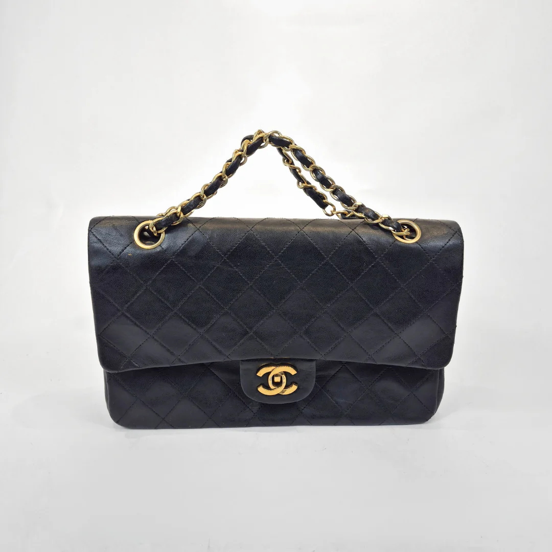 Black quilted handbag with gold chain and clasp on a white background
