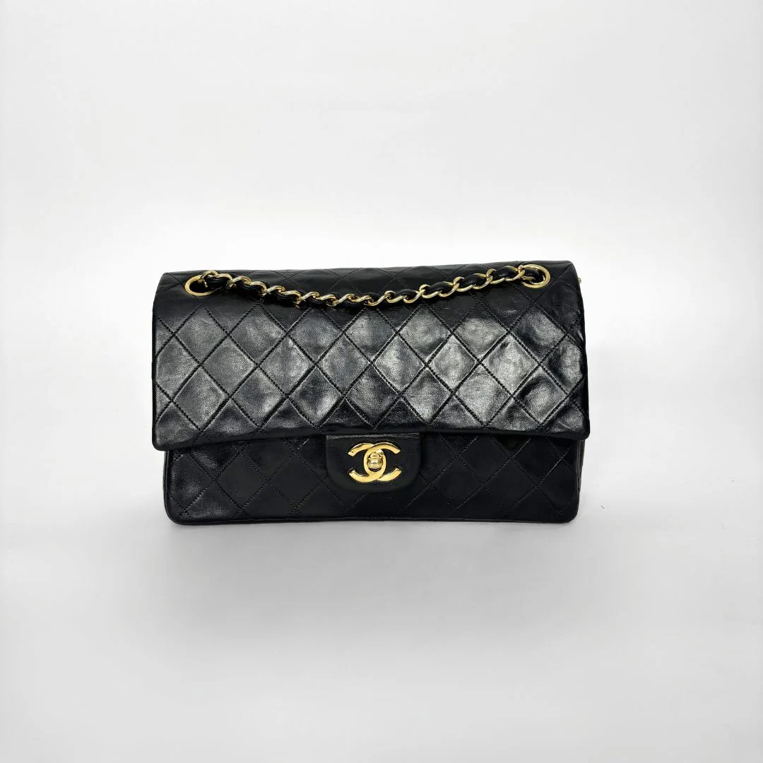 Black quilted handbag with gold chain and clasp on a white background