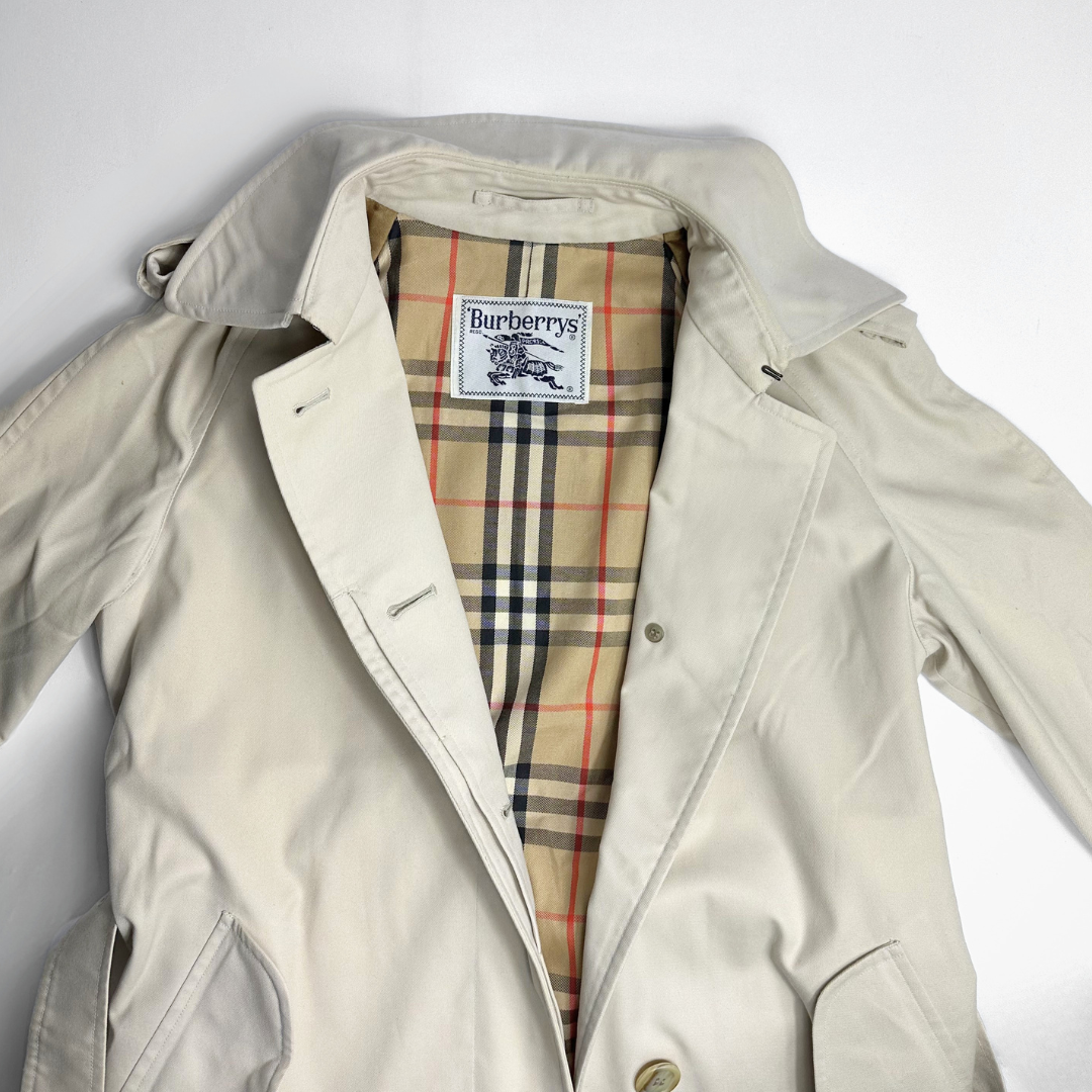 Beige trench coat with Burberry plaid lining on a white background