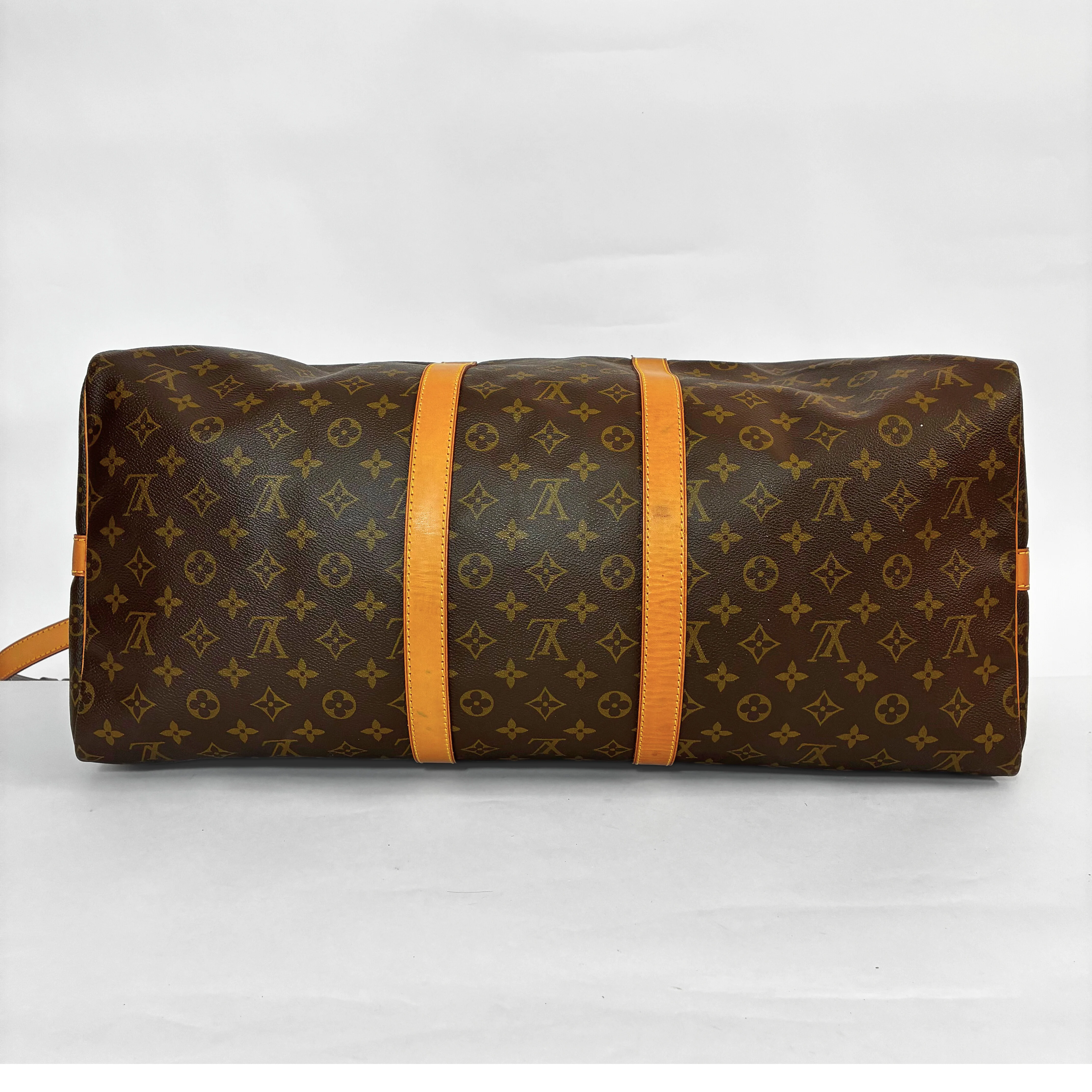 Brown leather bag with monogram pattern held open by black gloves on a white background
