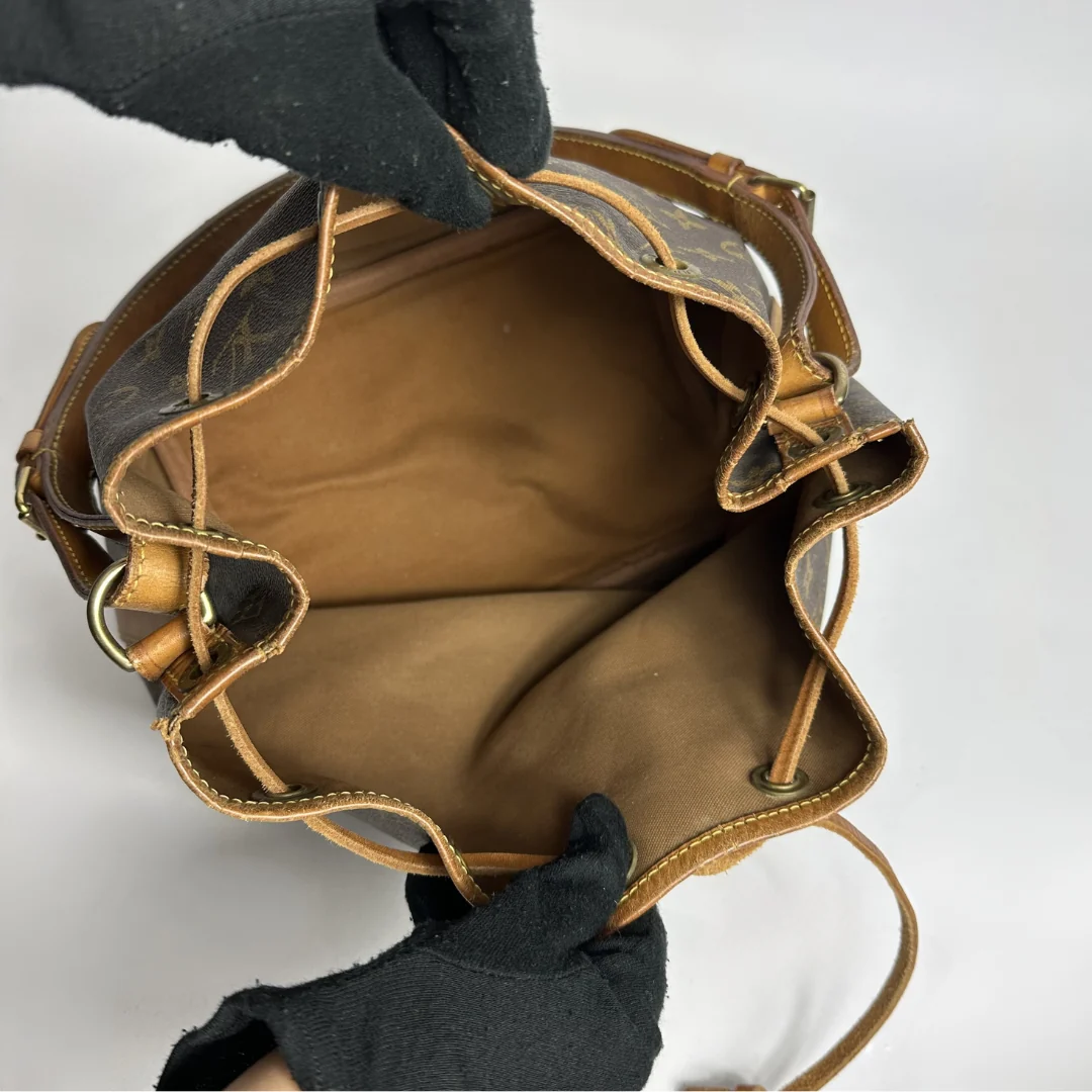 Brown leather bag with gold accents held by a gloved hand on a white background