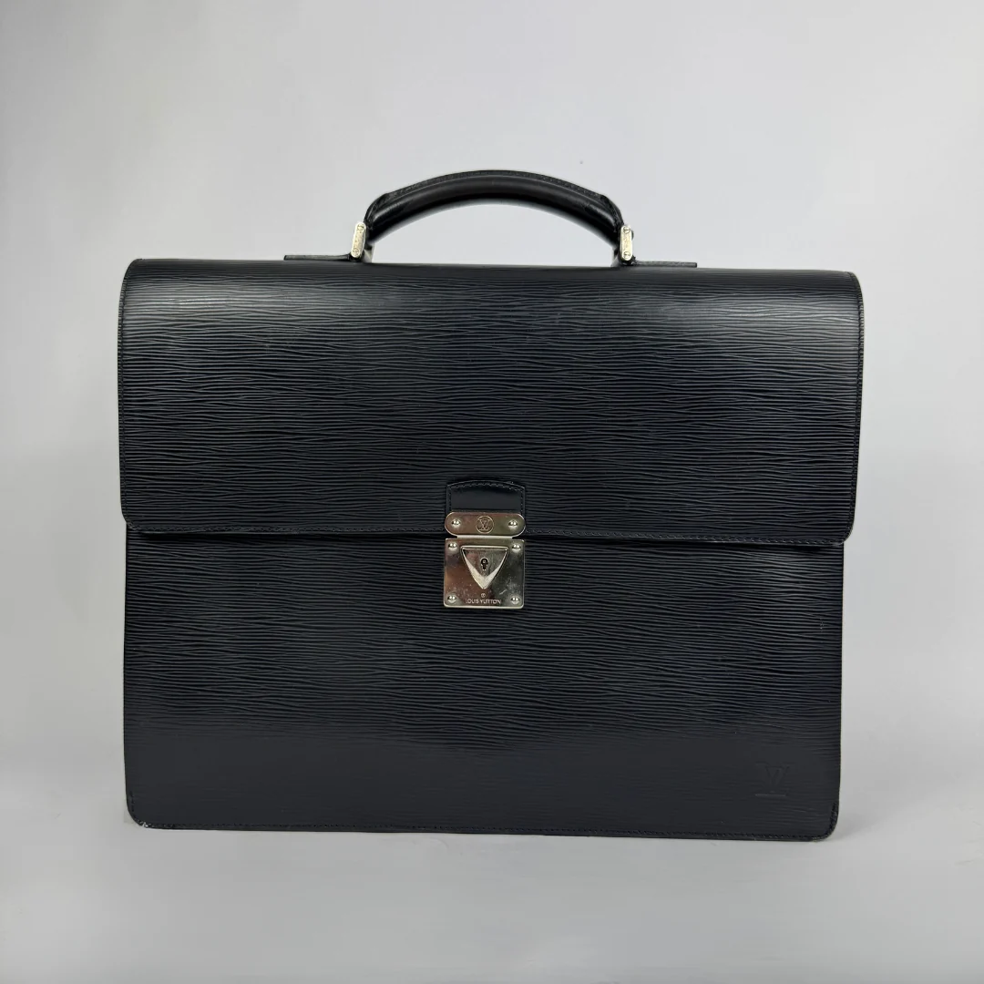 A black textured leather Louis Vuitton briefcase with a top handle and a silver-toned metal clasp on a light gray background.