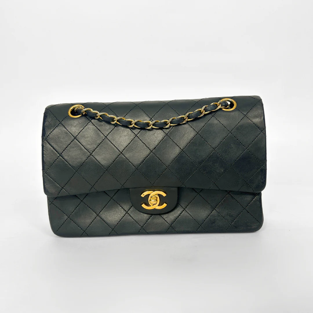 Black quilted handbag with gold chain and clasp on a white background