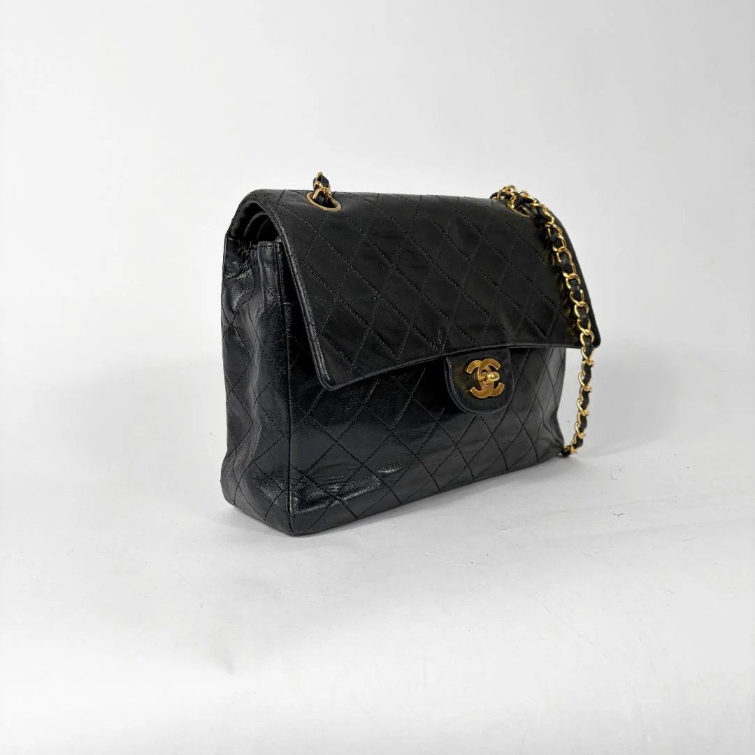 Black quilted handbag with gold chain and clasp on a white background