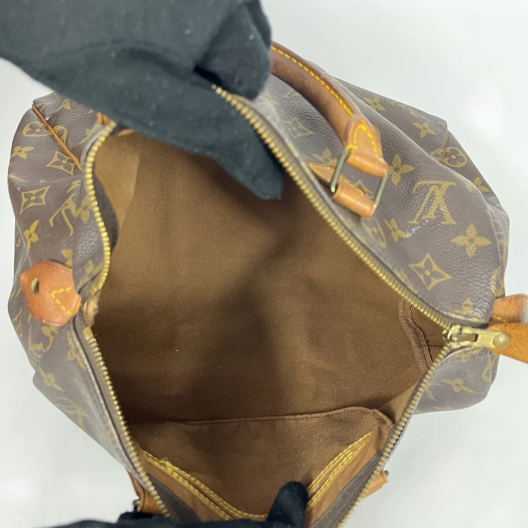 Louis Vuitton monogram canvas handbag shown open, with a black gloved hand holding the zipper tab. 