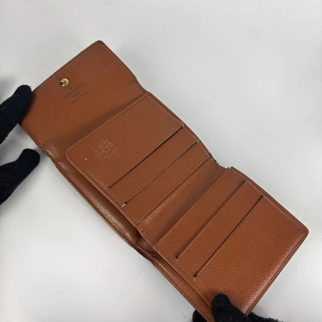 A brown textured leather wallet shown open, held by black-gloved hands against a plain white background.