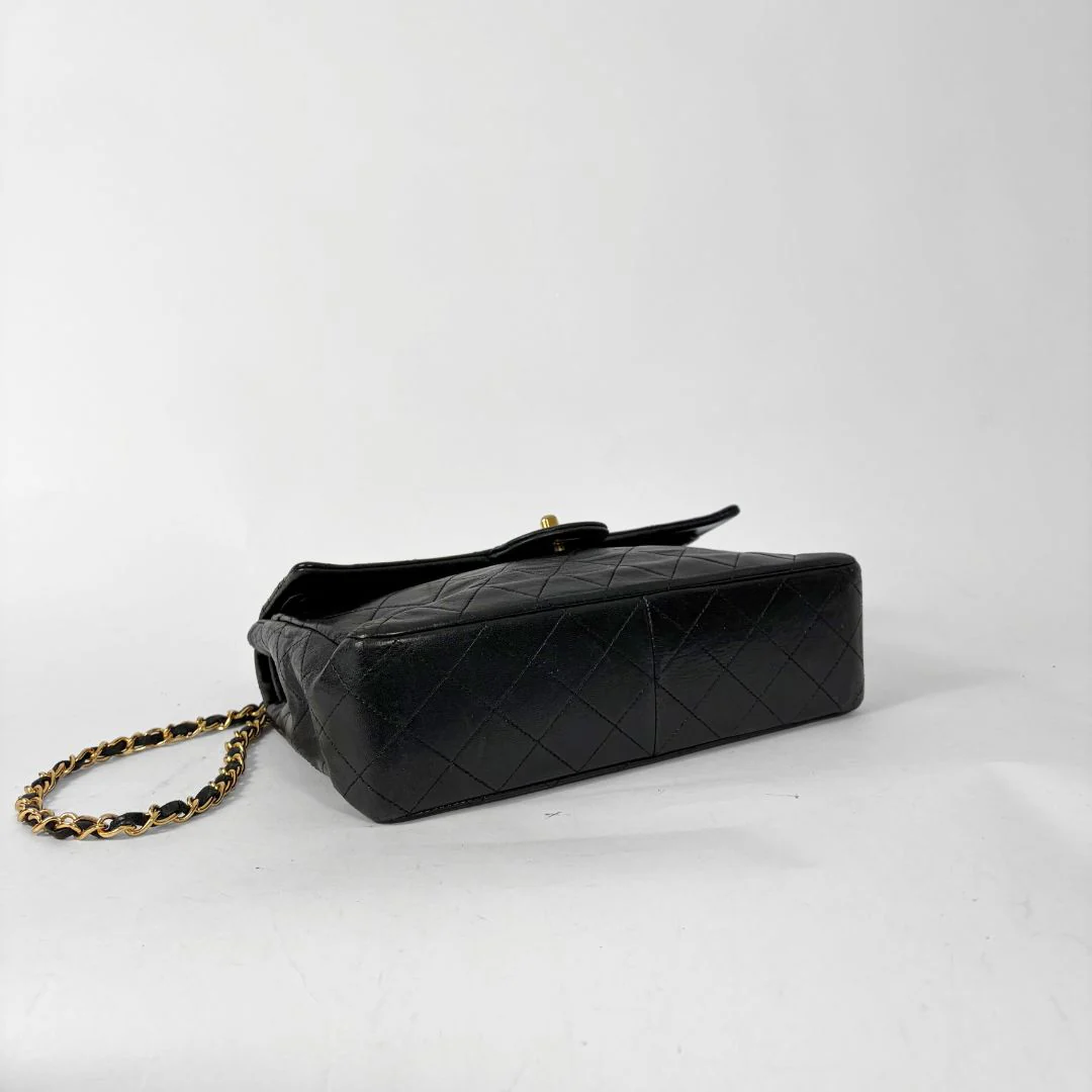Black quilted handbag with gold chain and clasp on a white background