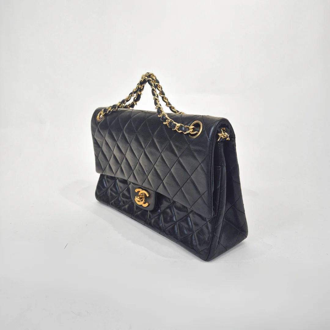 Black quilted handbag with gold chain and clasp on a white background